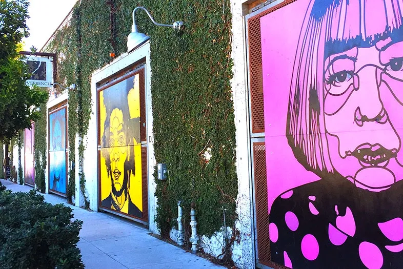 Colorful artwork on building doors with green vines and bright sunny day.