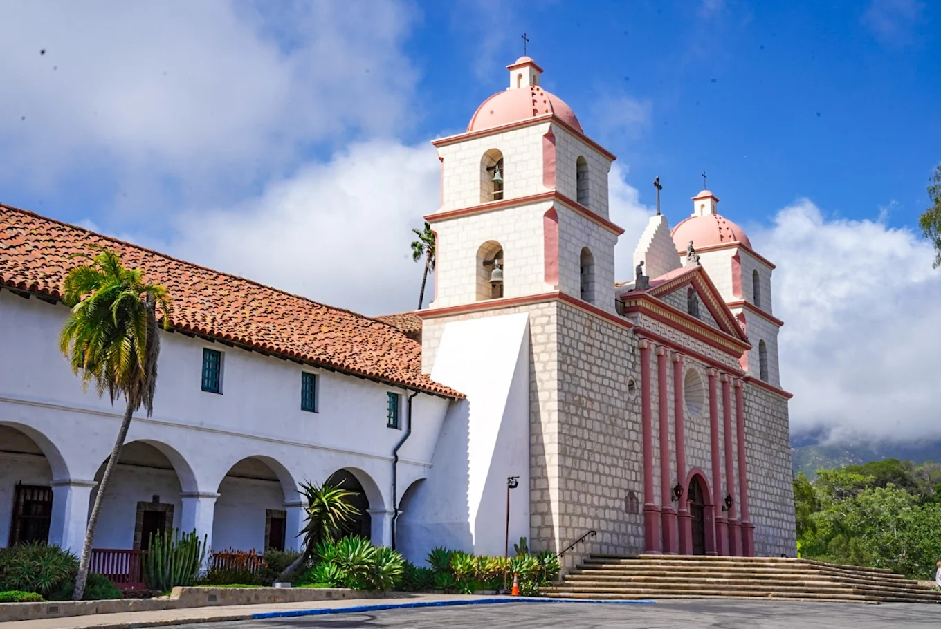 Front view of Old Mission Santa Barbara with a blue sky and spanish style building with green landscaping and steps.