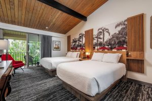 Ramada Santa Barbara Room with two beds and view of patio with green plants outside.