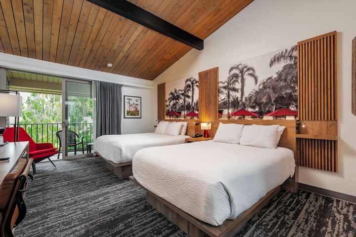 Ramada Santa Barbara Room with two beds and view of patio with green plants outside.