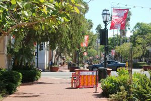 Downtown Santa Barabra with palm trees and flight post and an orange piano on the sidewalk with a car in the background.
