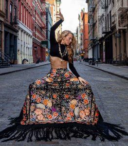 Siudy Garrido, woman posing in street while wearing a long, floral skirt with tassels.